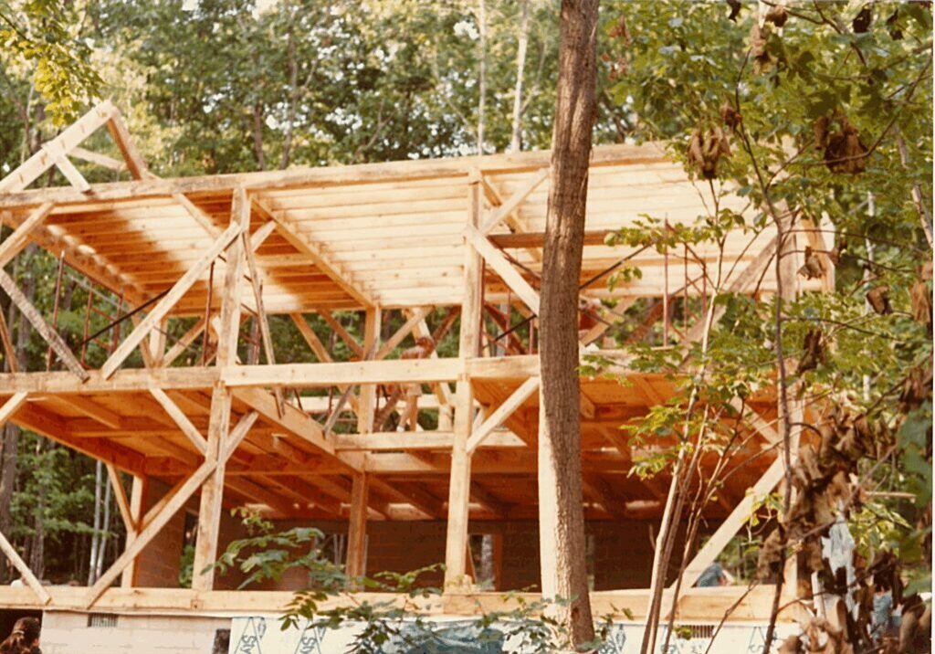 Wooden framework of a house under construction surrounded by trees.
